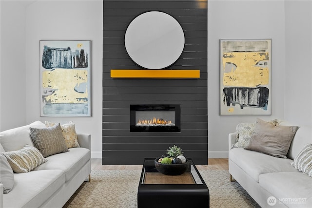 living area with wood finished floors, a large fireplace, and baseboards