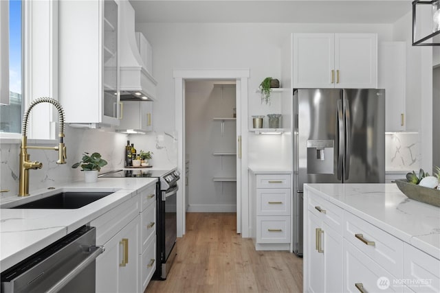 kitchen featuring appliances with stainless steel finishes, a sink, white cabinetry, light wood finished floors, and light stone counters