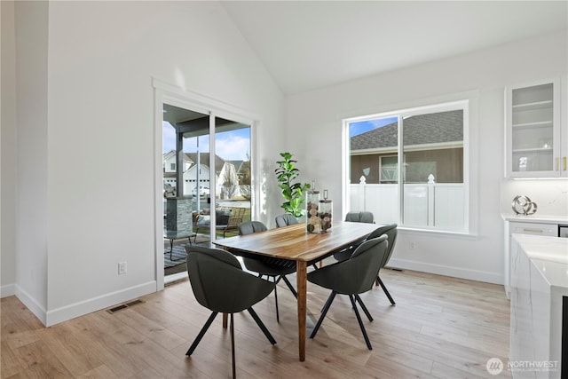 dining area with light wood finished floors, healthy amount of natural light, baseboards, and high vaulted ceiling