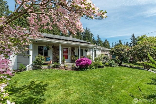view of front of home with covered porch, roof mounted solar panels, a front lawn, and a chimney