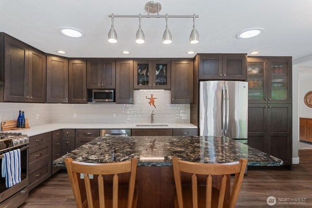 kitchen with stainless steel appliances, a sink, dark brown cabinetry, a kitchen breakfast bar, and recessed lighting
