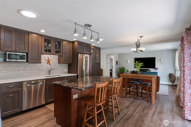 kitchen featuring stainless steel appliances, a sink, dark brown cabinetry, and glass insert cabinets