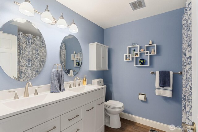 bathroom featuring toilet, wood finished floors, baseboards, and double vanity