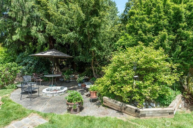 view of patio with an outdoor fire pit and a garden