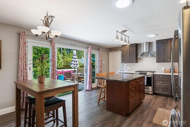 kitchen featuring stainless steel appliances, wall chimney exhaust hood, decorative backsplash, a chandelier, and dark brown cabinets