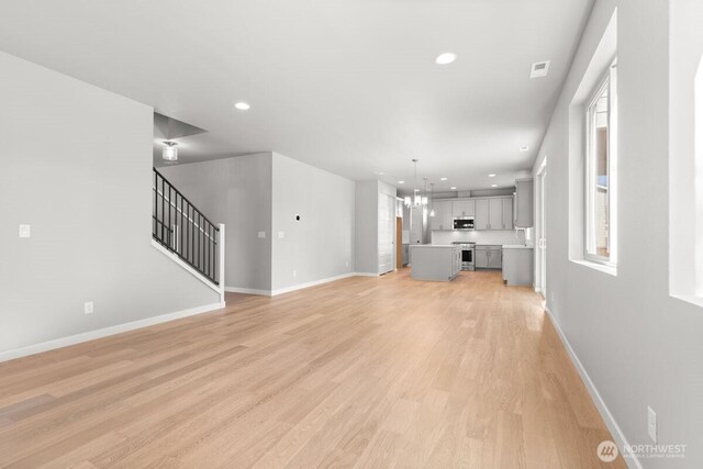 7332 284th St NW, Stanwood, WA 98292 - unfurnished living room with light wood-style flooring, recessed lighting, healthy amount of natural light, a chandelier, and stairway