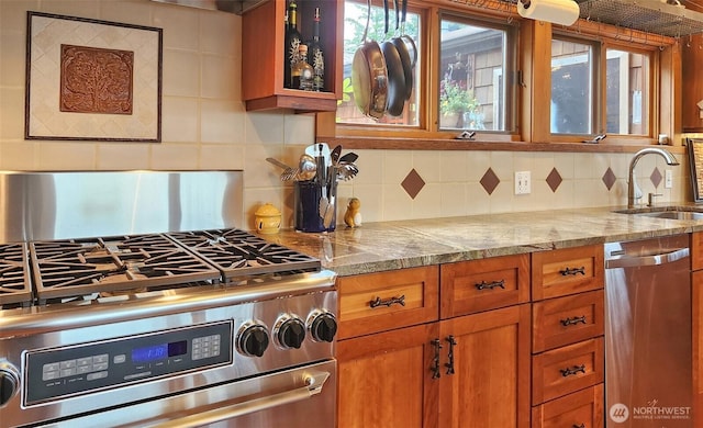 kitchen featuring stainless steel appliances, a sink, brown cabinetry, backsplash, and glass insert cabinets
