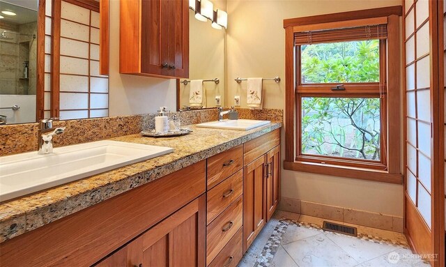 full bathroom with double vanity, a shower, and baseboards