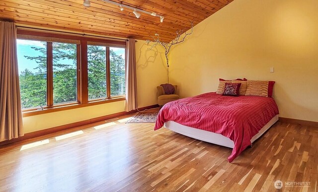 bedroom with rail lighting, baseboards, wood finished floors, vaulted ceiling, and wooden ceiling