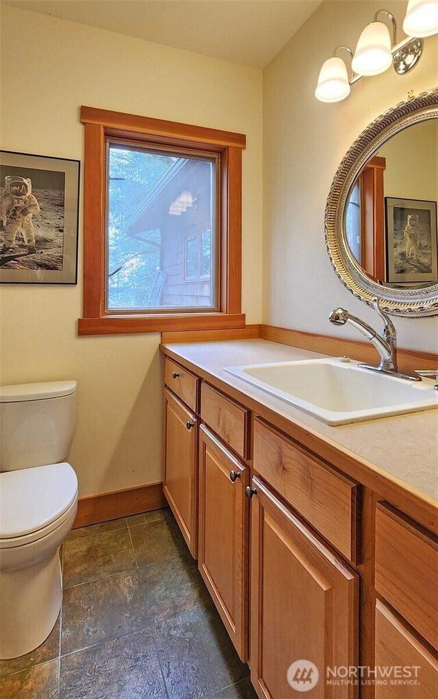 bathroom with toilet, baseboards, vanity, and stone finish flooring