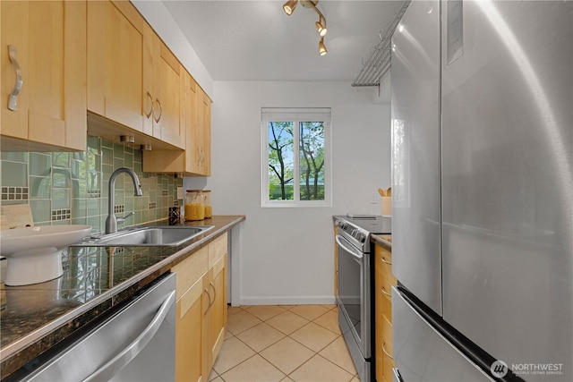 kitchen featuring stainless steel appliances, a sink, light brown cabinets, backsplash, and dark countertops