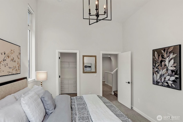 carpeted bedroom featuring a towering ceiling, a chandelier, baseboards, and a spacious closet