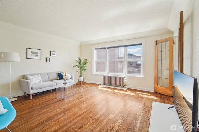 living area with radiator heating unit, wood finished floors, and baseboards