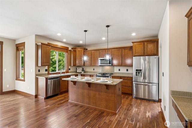 13809 172nd Pl E, Puyallup, WA 98374 - kitchen featuring appliances with stainless steel finishes, brown cabinets, dark wood-type flooring, a kitchen island, and decorative light fixtures