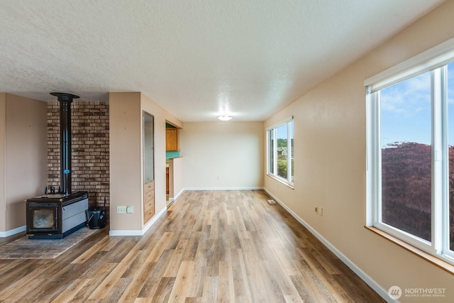 1068 Vista Del Monte, Camano Island, WA 98282 - unfurnished living room with a wood stove, light wood-style flooring, a textured ceiling, and baseboards