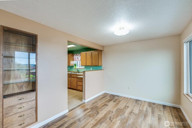 1068 Vista Del Monte, Camano Island, WA 98282 - kitchen featuring a textured ceiling, light wood finished floors, brown cabinetry, baseboards, and a sink