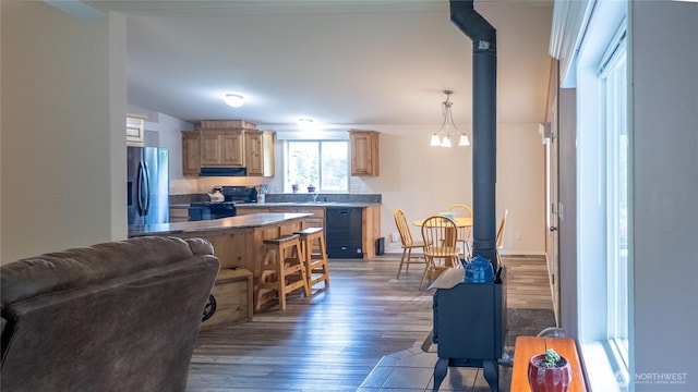 kitchen featuring black appliances, range hood, a wood stove, wood finished floors, and light brown cabinets