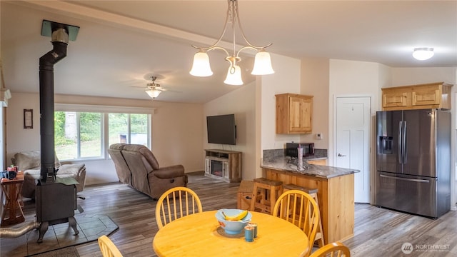 dining space featuring a wood stove, wood finished floors, ceiling fan, lofted ceiling, and a fireplace