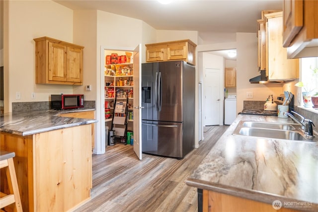 kitchen featuring stainless steel fridge with ice dispenser, a sink, washer / clothes dryer, light wood-style flooring, and a peninsula
