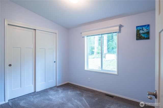 unfurnished bedroom featuring dark colored carpet, vaulted ceiling, a closet, and baseboards