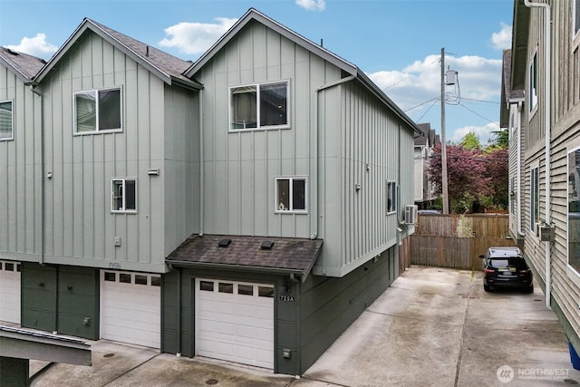 view of side of property featuring board and batten siding, an attached garage, a shingled roof, fence, and concrete driveway