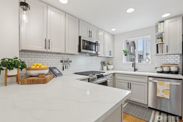 kitchen featuring stainless steel appliances, a sink, tasteful backsplash, light stone countertops, and open shelves