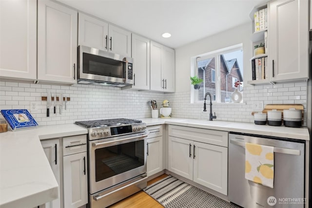 kitchen with appliances with stainless steel finishes, a sink, decorative backsplash, open shelves, and light stone counters
