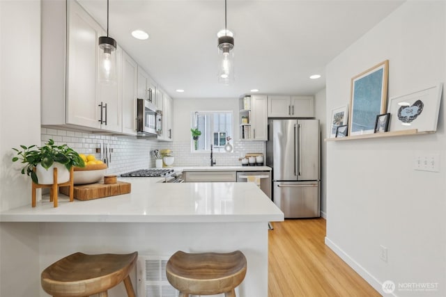 kitchen with stainless steel appliances, a peninsula, backsplash, light wood-style flooring, and pendant lighting