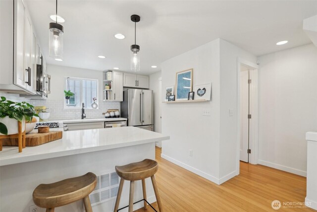 kitchen featuring baseboards, light wood-type flooring, tasteful backsplash, a kitchen bar, and recessed lighting