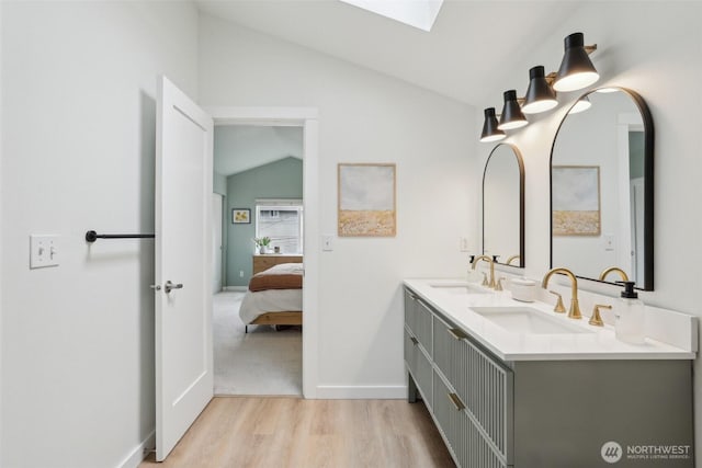 ensuite bathroom featuring lofted ceiling, a skylight, wood finished floors, baseboards, and double vanity