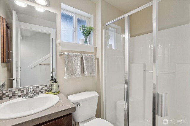 bathroom featuring decorative backsplash, a stall shower, vanity, and toilet