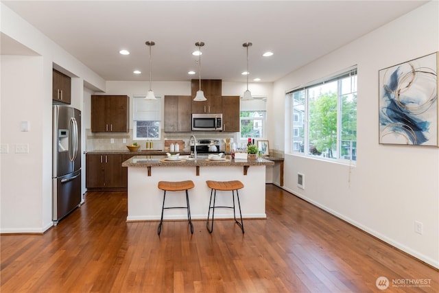 kitchen featuring appliances with stainless steel finishes, a breakfast bar, backsplash, dark wood finished floors, and a kitchen island with sink