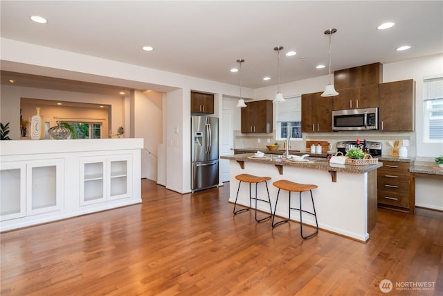 kitchen with stainless steel appliances, a breakfast bar, decorative backsplash, dark wood finished floors, and a center island with sink