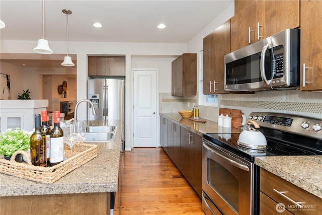 kitchen with appliances with stainless steel finishes, a sink, light wood finished floors, hanging light fixtures, and brown cabinets