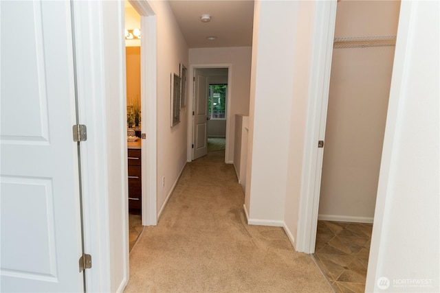 hallway featuring light carpet and baseboards