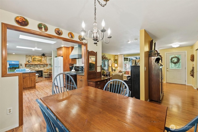 2124 213th Street Ct E, Spanaway, WA 98387 - dining room with light wood-style flooring, a stone fireplace, a chandelier, a ceiling fan, and baseboards