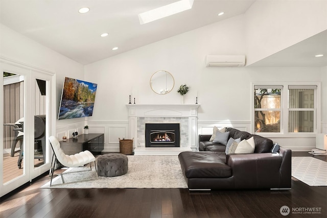 living area with a wall unit AC, dark wood-type flooring, a premium fireplace, wainscoting, and a decorative wall