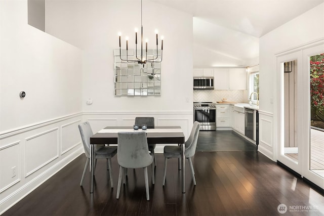 dining room with a chandelier, dark wood-style flooring, wainscoting, and a decorative wall