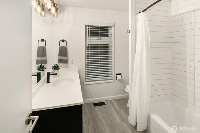 full bathroom featuring toilet, vanity, wood finished floors, shower / bath combination with curtain, and baseboards
