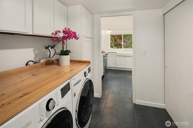 laundry area featuring separate washer and dryer, dark tile patterned floors, cabinet space, and baseboards