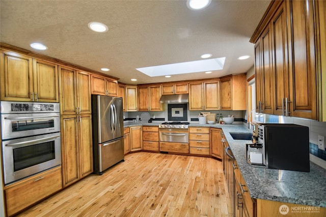 10910 114th Ave SW, Tacoma, WA 98498 - kitchen featuring appliances with stainless steel finishes, a skylight, under cabinet range hood, brown cabinetry, and recessed lighting