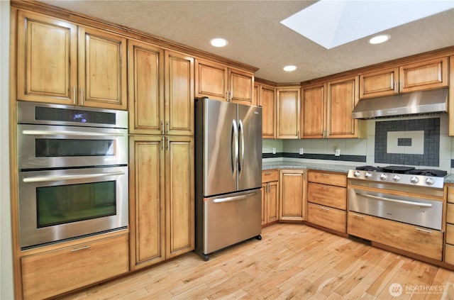 10910 114th Ave SW, Tacoma, WA 98498 - kitchen featuring appliances with stainless steel finishes, under cabinet range hood, a warming drawer, a skylight, and light wood-style floors