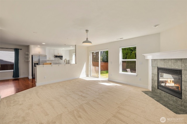unfurnished living room featuring carpet, a fireplace, a sink, baseboards, and recessed lighting