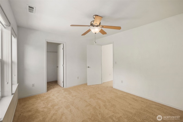 unfurnished bedroom with light carpet, a spacious closet, ceiling fan, a closet, and baseboards