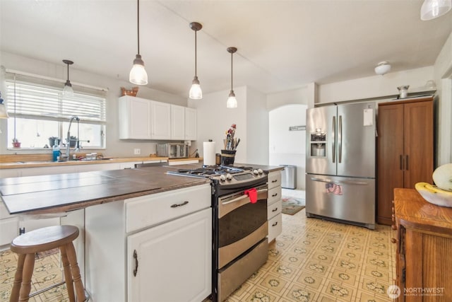 12623 Douglas Rd, Yakima, WA 98908 - kitchen featuring appliances with stainless steel finishes, white cabinets, arched walkways, a sink, and decorative light fixtures