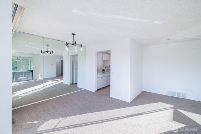 unfurnished living room featuring carpet flooring, a chandelier, a sink, and a textured ceiling