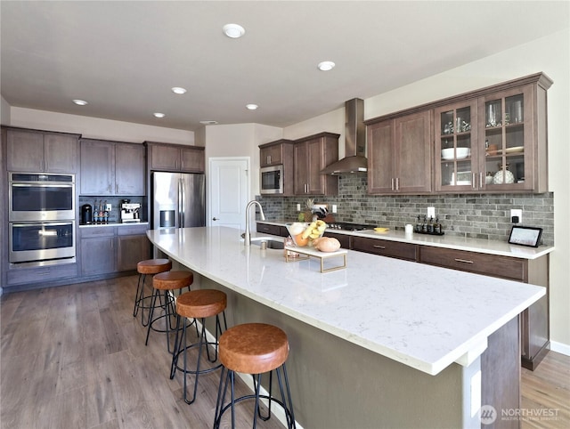 9932 15th Pl SE, Lake Stevens, WA 98258 - kitchen featuring wall chimney exhaust hood, stainless steel appliances, a breakfast bar, decorative backsplash, and light wood-style flooring