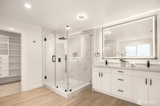 bathroom with a marble finish shower, wood finished floors, a spacious closet, double vanity, and recessed lighting