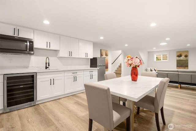dining room featuring wine cooler, light wood-style flooring, stairway, wet bar, and recessed lighting