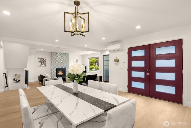 dining space featuring a warm lit fireplace, a wall unit AC, recessed lighting, a chandelier, and baseboards